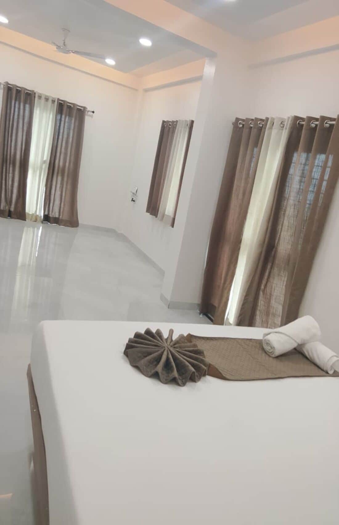 A hotel room with a large bed, a ceiling fan, and curtains on the windows.