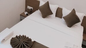 A neatly made bed with a white duvet, brown pillows, and a decorative brown pillow on the side. - Jayesh Lodging (Shirur)