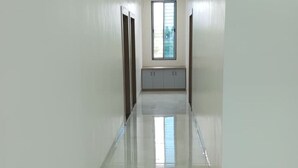 A corridor with a shiny floor, a window at the end, and a bench with cabinets. - Jayesh Lodging (Shirur)