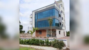 A modern multi-story building with a flat roof, large windows, and a gated entrance. - Jayesh Lodging (Shirur)