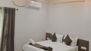 A modern bedroom with a bed, air conditioning unit, and recessed lighting. - Jayesh Lodging (Shirur)