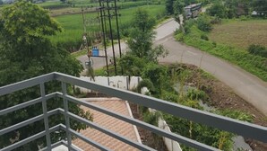 A balcony with a view of a rural landscape, including fields, a road, and power lines. - Jayesh Lodging (Shirur)