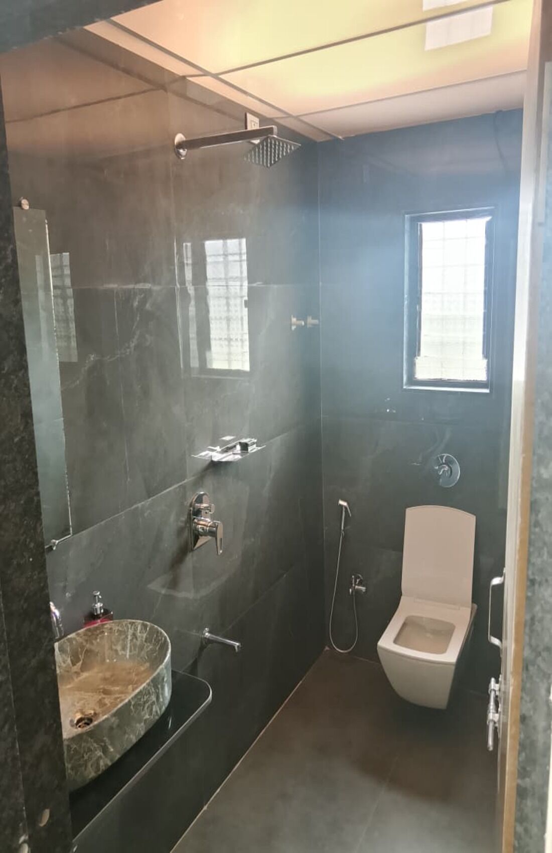 A bathroom with a marble sink, a toilet, a shower, and a window.