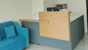 A reception area with a blue sofa, a wooden reception desk, and a ceiling fan. - Jayesh Lodging (Shirur)