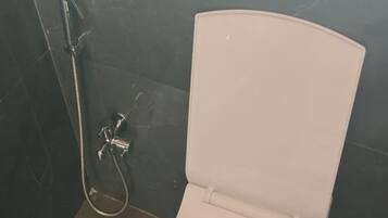 A toilet with a bidet attachment and a showerhead in a bathroom with dark tiled walls.