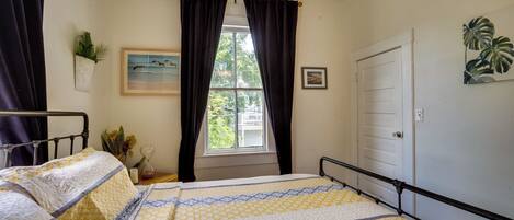 Une chambre à coucher avec un lit, une fenêtre avec des rideaux, un ventilateur de plafond, une porte et une plante fixée au mur.