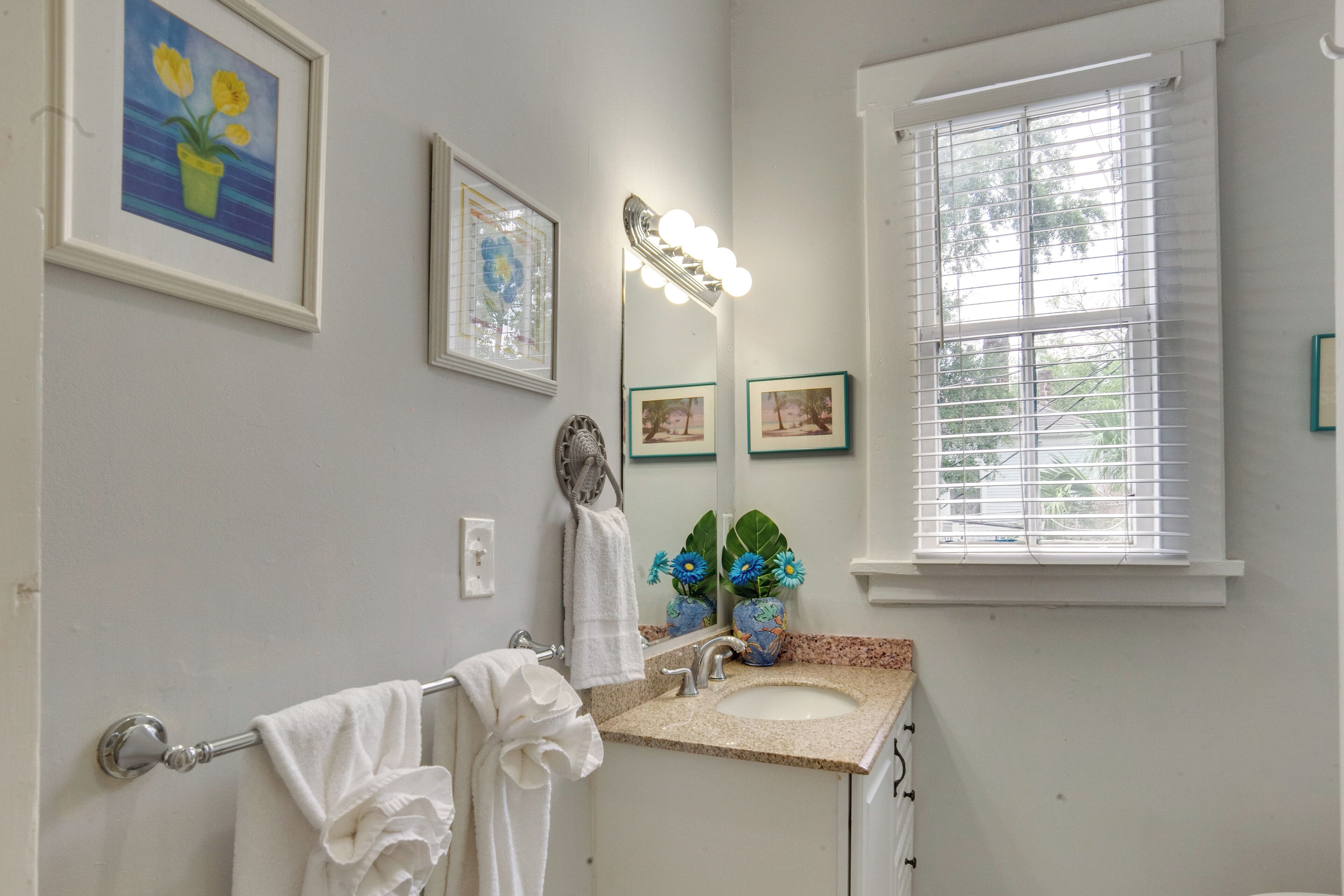 A bathroom with a sink, vanity mirror, and two framed pictures on the wall.