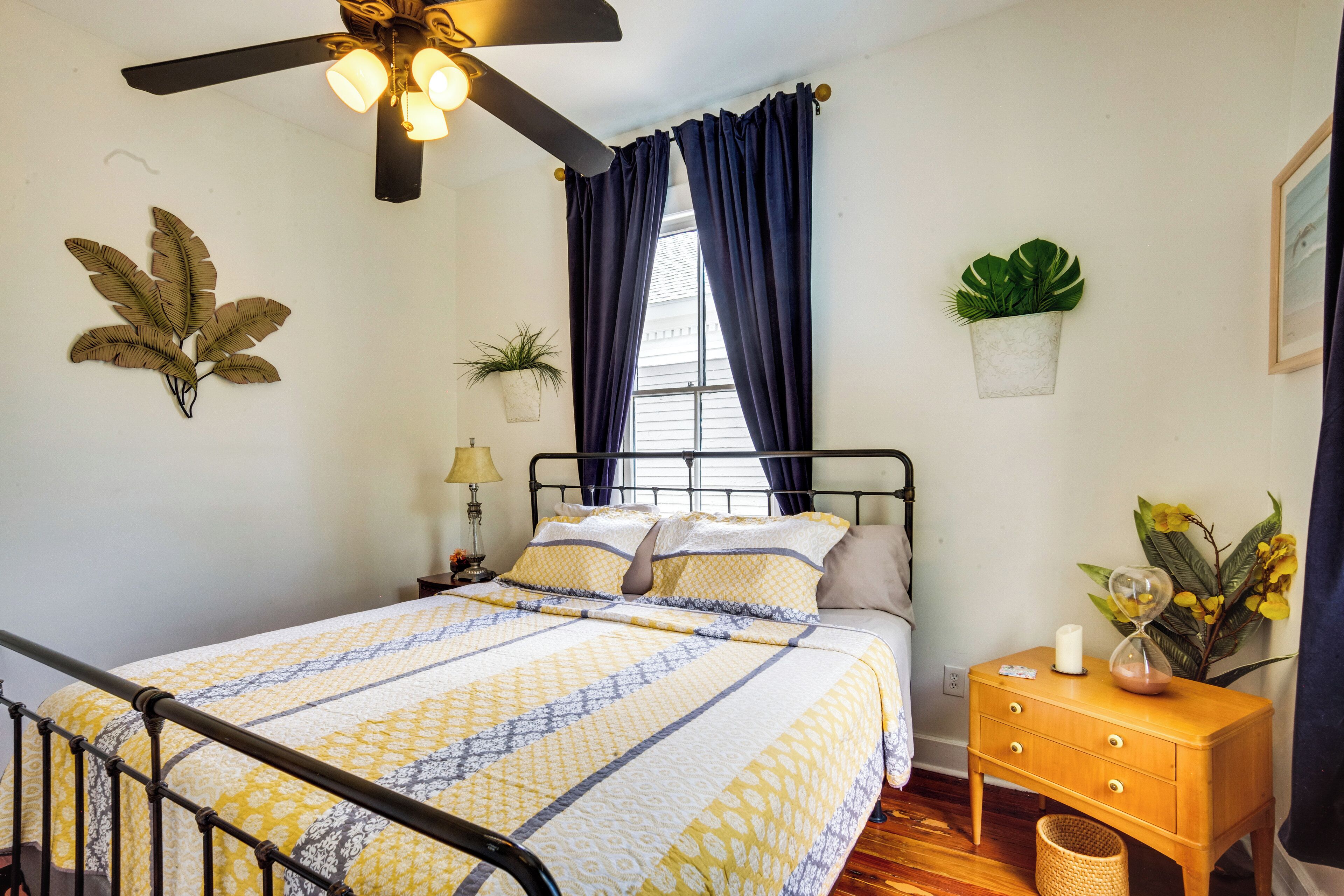 A bedroom with a bed, a nightstand, a lamp, a ceiling fan, and a window with curtains.
