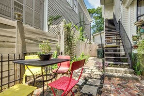 Eine Terrasse mit Tisch und Stühlen, ein Holzzaun, ein Pflasterweg und eine Treppe, die zu einer zweiten Ebene führt.