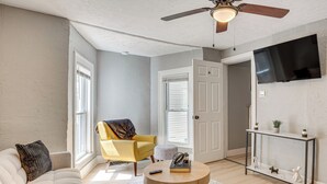 Una sala de estar con sofá, sillón, una mesita redonda y un televisor montado en la pared.