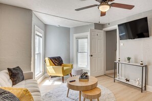 A living room with a sofa, armchair, round coffee table, and a TV mounted on the wall. - Walk to University of Akron! Game Day Getaway (Akron)