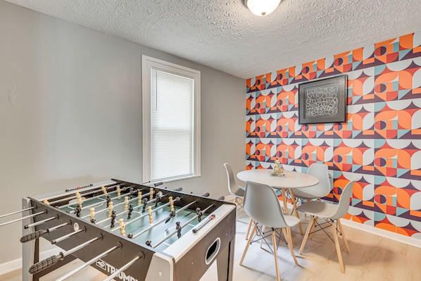 A room with a foosball table, a dining table with chairs, and a colorful geometric wall mural. - Walk to University of Akron! Game Day Getaway (Akron)