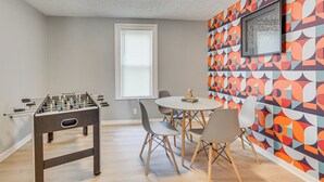 Una habitación con mesa de futbolín, una mesa redonda de comedor con sillas y un llamativo mural geométrico en la pared.