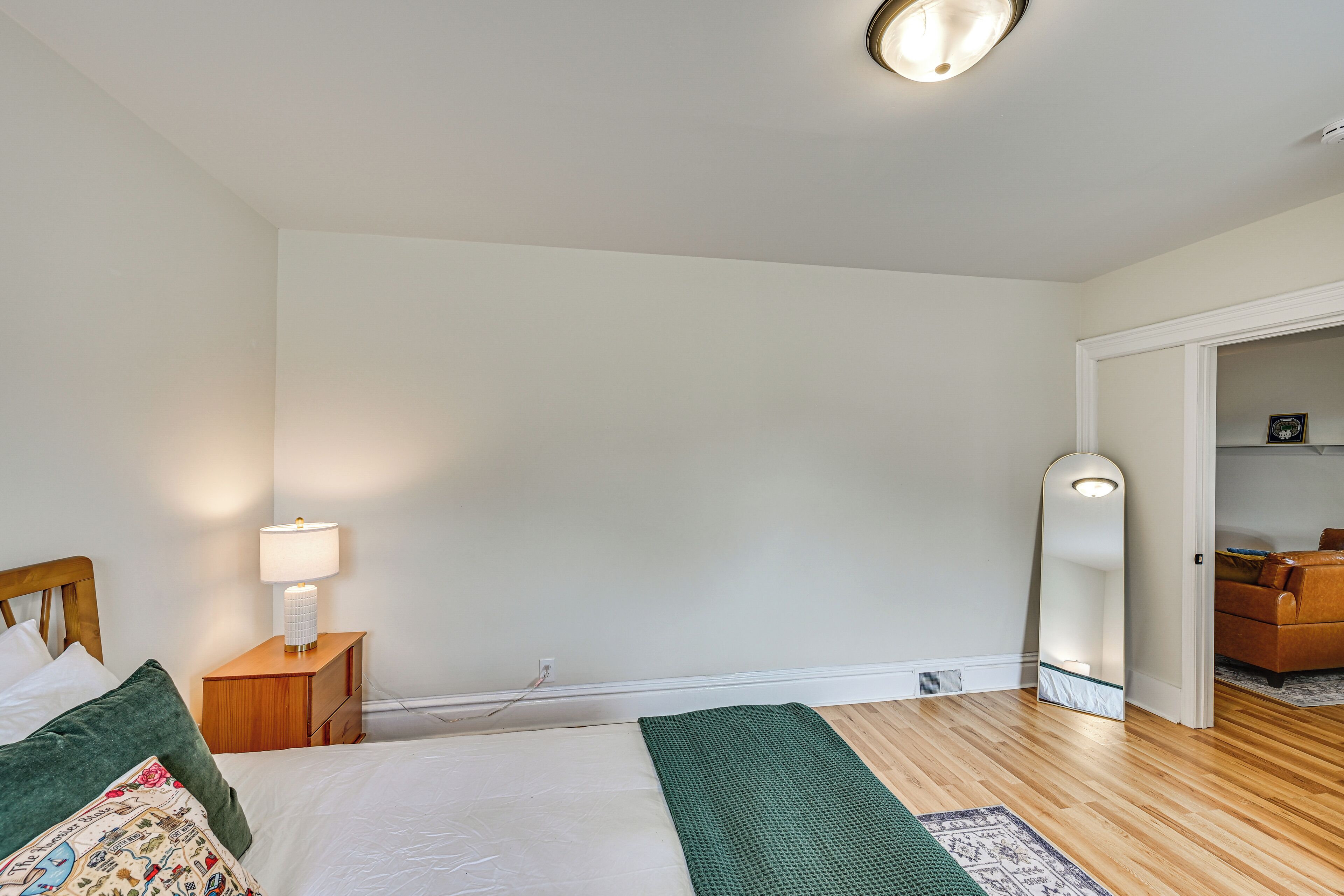A bedroom with a bed, bedside table, lamp, and a mirror.