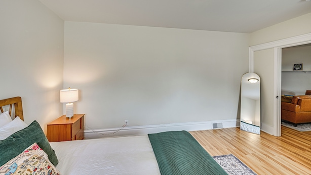 A bedroom with a bed, bedside table, lamp, and a mirror.