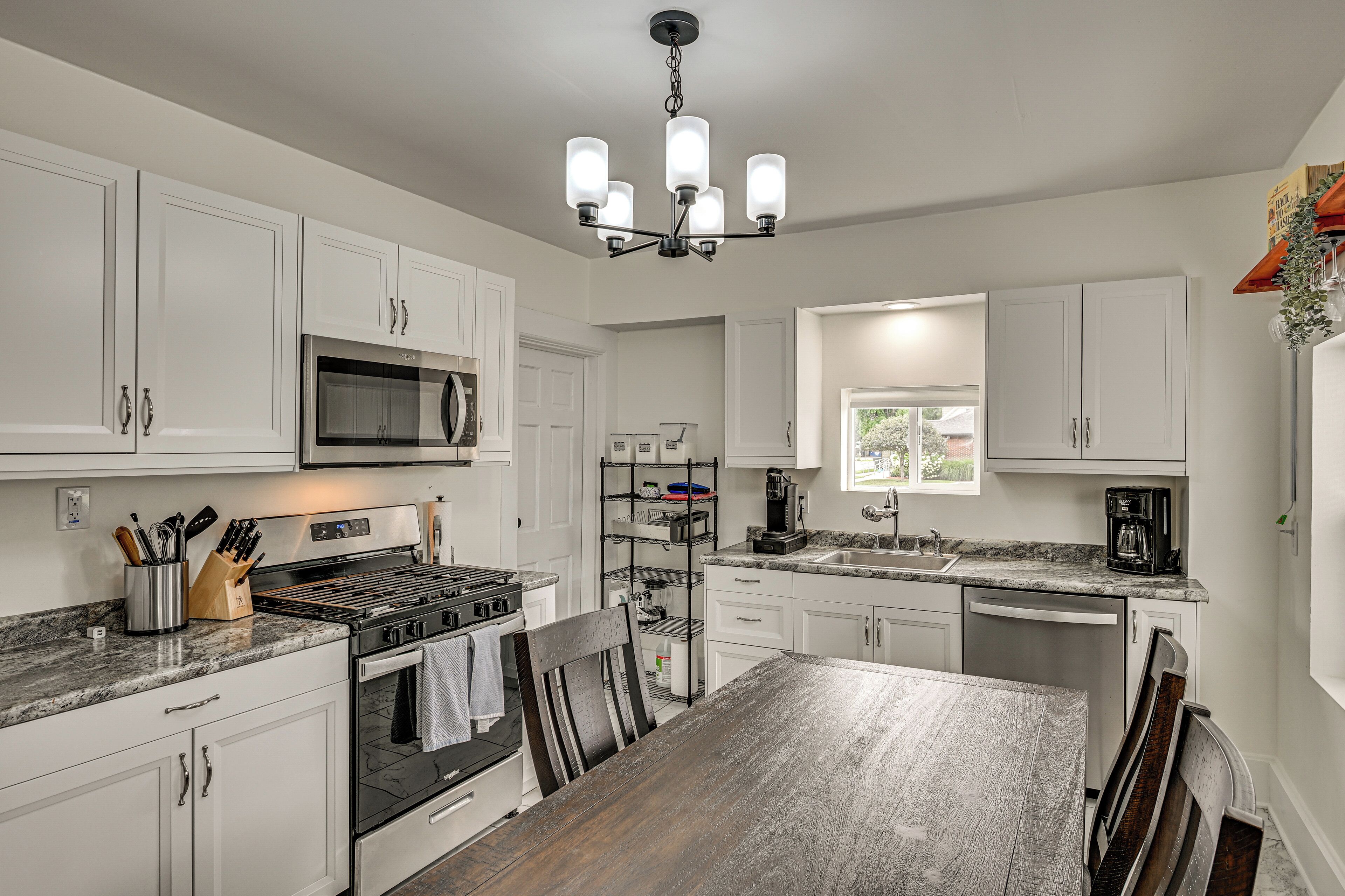 A modern kitchen with white cabinets, stainless steel appliances, a granite countertop, and a wooden dining table.