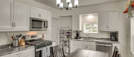 Una cocina moderna con armarios blancos, electrodomésticos de acero inoxidable, encimera de granito y una mesa de comedor de madera.