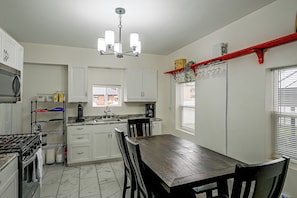 Een keuken met witte kastjes, een zwart aanrecht, een houten eettafel en een kroonluchter.
