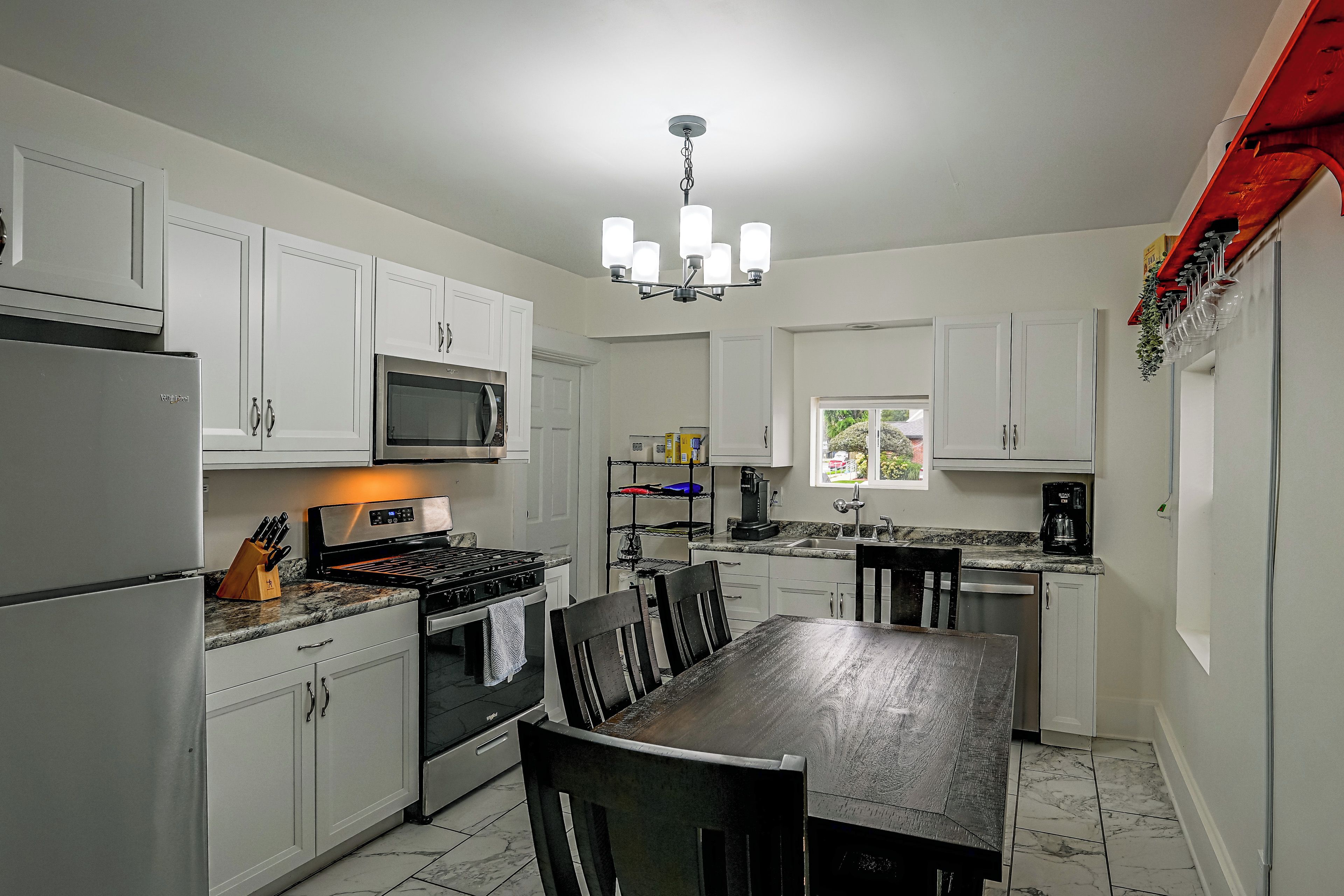 A modern kitchen with white cabinetry, a stainless steel refrigerator, a microwave, a gas stove, and a dining area with a table and chairs.