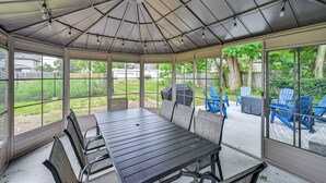 A covered patio with a table and chairs, large windows, and a view of the backyard.