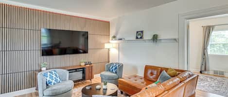 A modern living room with a flat-screen TV, two armchairs, a sofa, a coffee table, and a bookshelf.