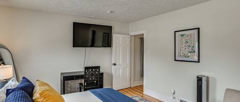 A bedroom with a bed, a TV mounted on the wall, a desk, a chair, and a framed map on the wall.