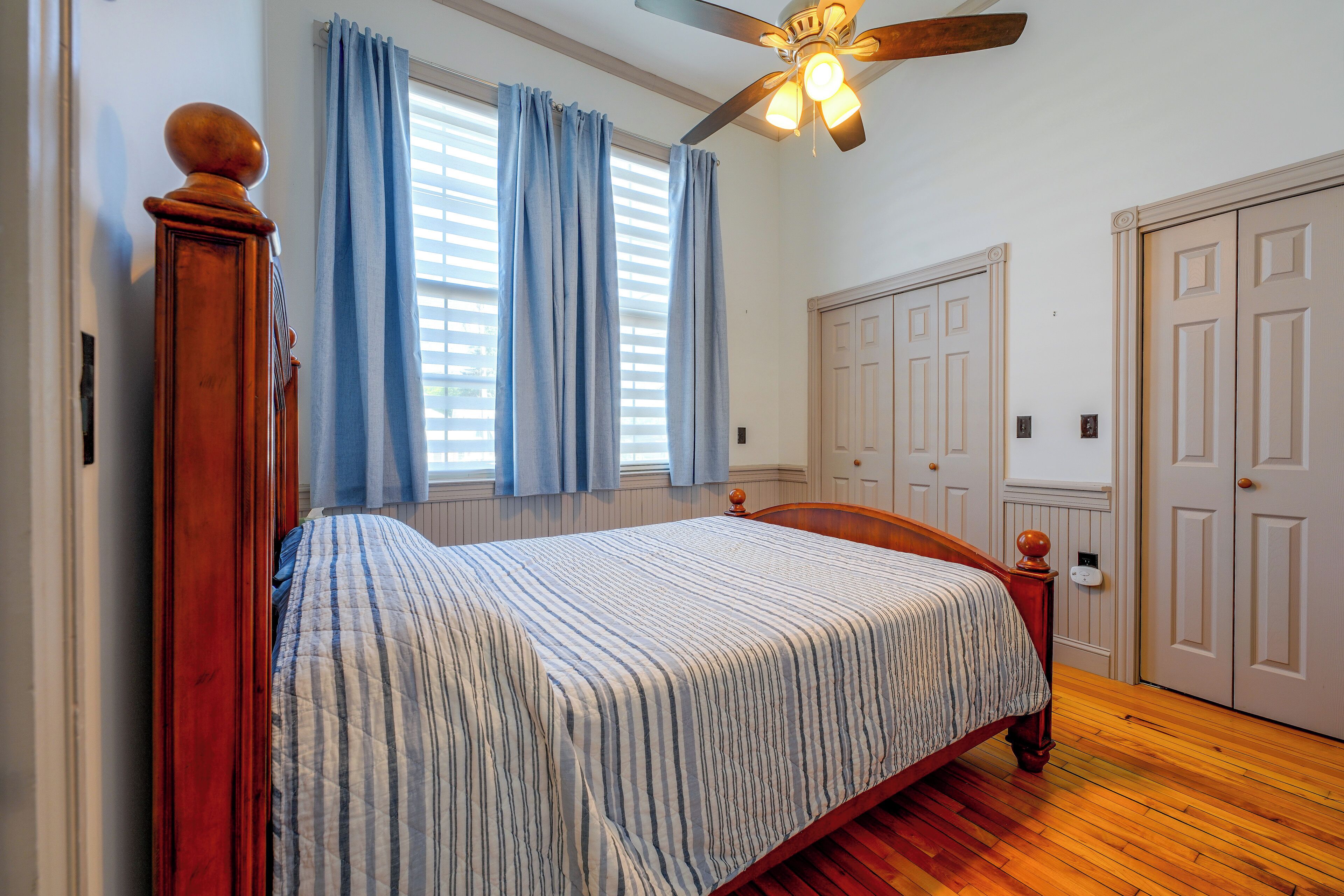 A bedroom with a bed, a ceiling fan, a window with curtains, and a door.