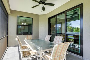 Eine überdachte Terrasse mit Glastür zum Balkon, einem Deckenventilator und einem Tisch mit Stühlen.