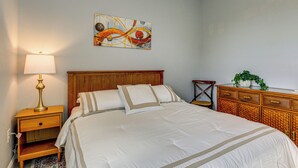 A neatly made bed with a wooden headboard, a bedside table with a lamp, a decorative wall piece, and a wicker side table with a plant. - 6 Mi to Port Charlotte Beach Park! Family Getaway (Port Charlotte)