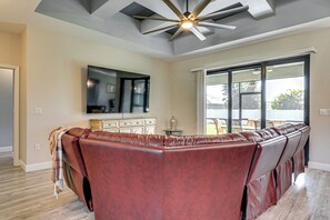 A living room with a long brown leather sofa, a flat-screen TV mounted on the wall, and a ceiling fan. - 6 Mi to Port Charlotte Beach Park! Family Getaway (Port Charlotte)