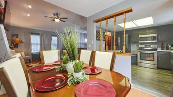 A dining area with a wooden table set for four, a ceiling fan, and a view into a kitchen with modern appliances.