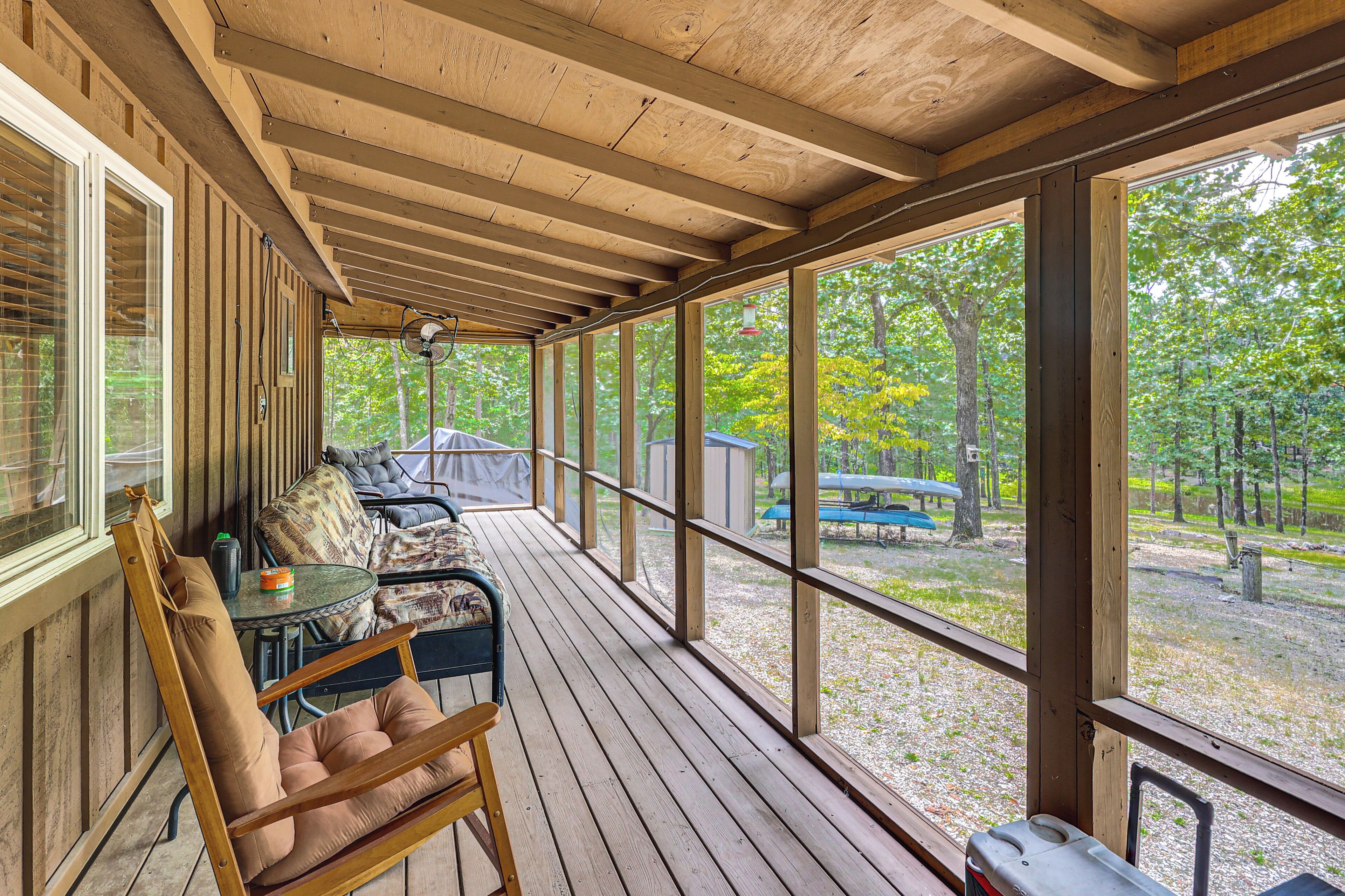 A wooden deck with a table and chairs, overlooking a wooded area with boats.