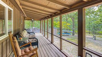 A wooden deck with a table and chairs, overlooking a wooded area with boats.