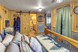 A cabin interior with a wooden floor, a sofa, a dining table, and a kitchen area. - Adventure Basecamp Near Lake Ouachita! (Mount Ida)