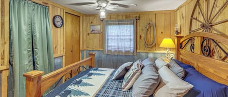Una habitación con cama, paredes de madera, ventilador de techo, reloj y ventana con cortinas.