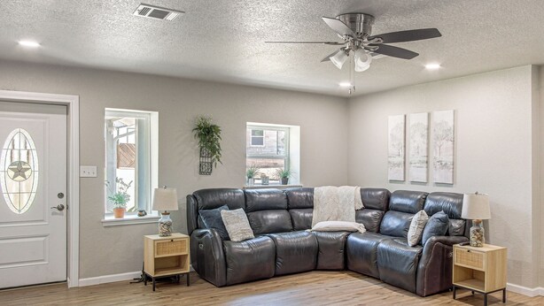 A modern living room with a sectional sofa, two side tables, a ceiling fan, and a door with a decorative glass panel. - Boat Ramp Access! Canalfront Granbury Escape (Granbury)