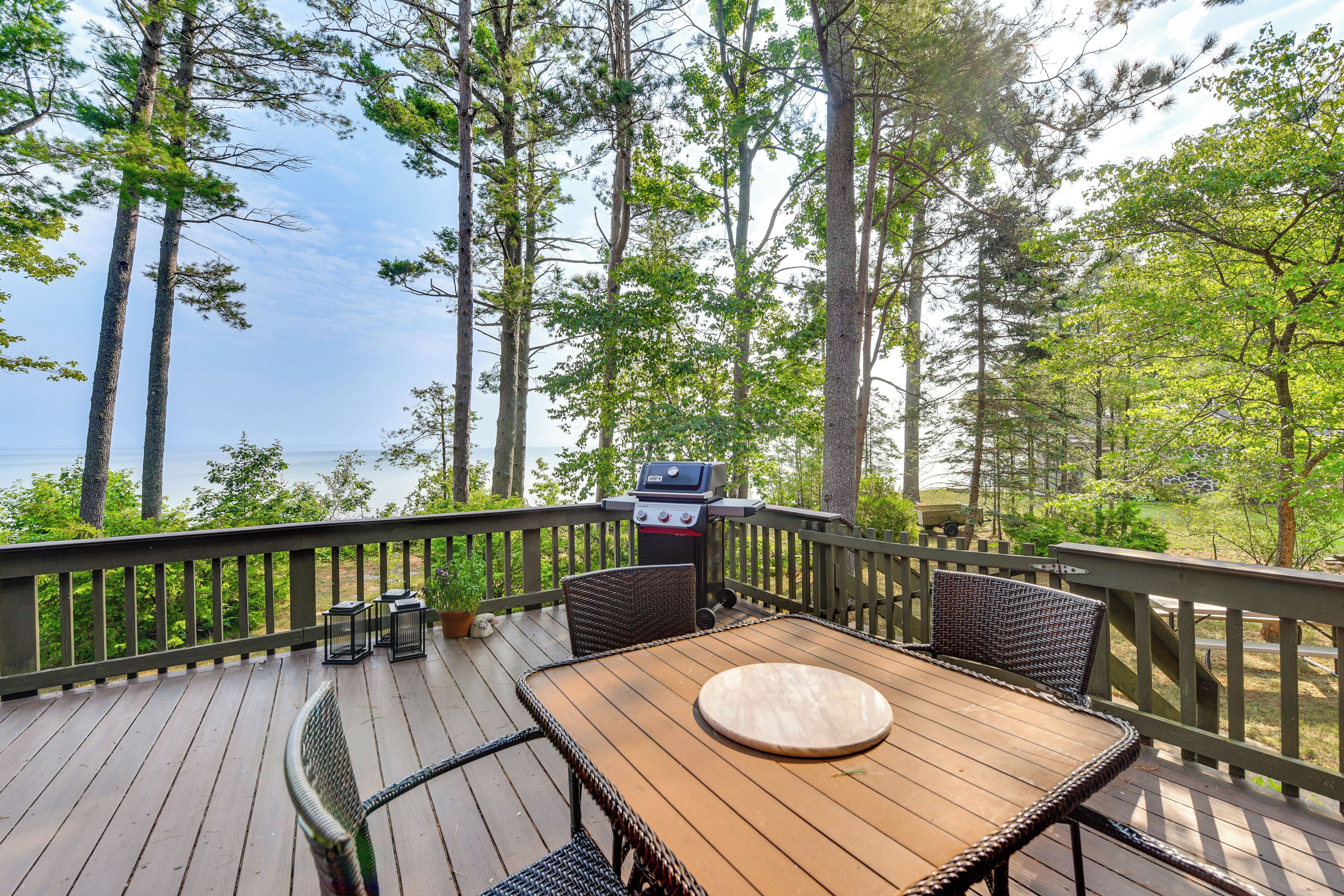 A wooden deck with a table and chairs, overlooking a body of water and surrounded by trees.