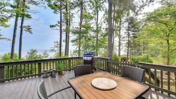 Une terrasse en bois avec une table et des chaises, donnant sur une étendue d’eau et entourée d’arbres.