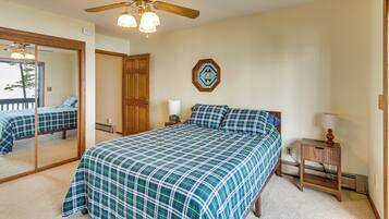 A bedroom with a large bed, a ceiling fan, a mirror, a nightstand, and a window with a decorative frame.
