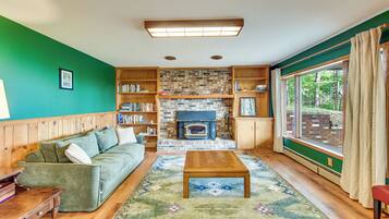 A cozy living room with a green wall, wooden furniture, a fireplace, and a large window with curtains.