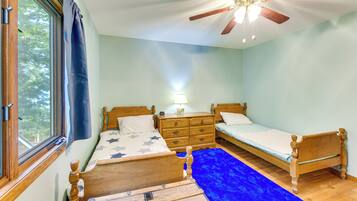 Une chambre à coucher avec un lit, une commode, une table de chevet, un tapis bleu et un ventilateur de plafond.