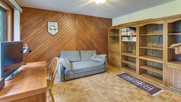 A room with a herringbone wooden floor, a grey sofa, a wooden cabinet with board games, and a television on a wooden desk.