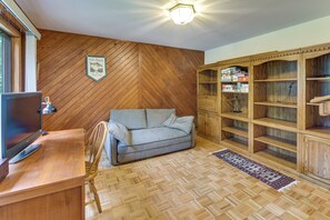 Een kamer met een visgraat parketvloer, een grijze bank, een houten kast met gezelschapsspellen, en een televisie op een houten bureau.