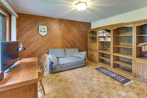 Una habitación con suelo de madera tipo espiga, un sofá gris, un mueble de madera con juegos de mesa y un televisor sobre un escritorio de madera.
