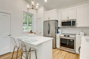 A modern kitchen with white cabinetry, stainless steel appliances, and a central island with bar stools. - Newly Built Home, Fall Foliage, Nearby Vineyard (South Haven)