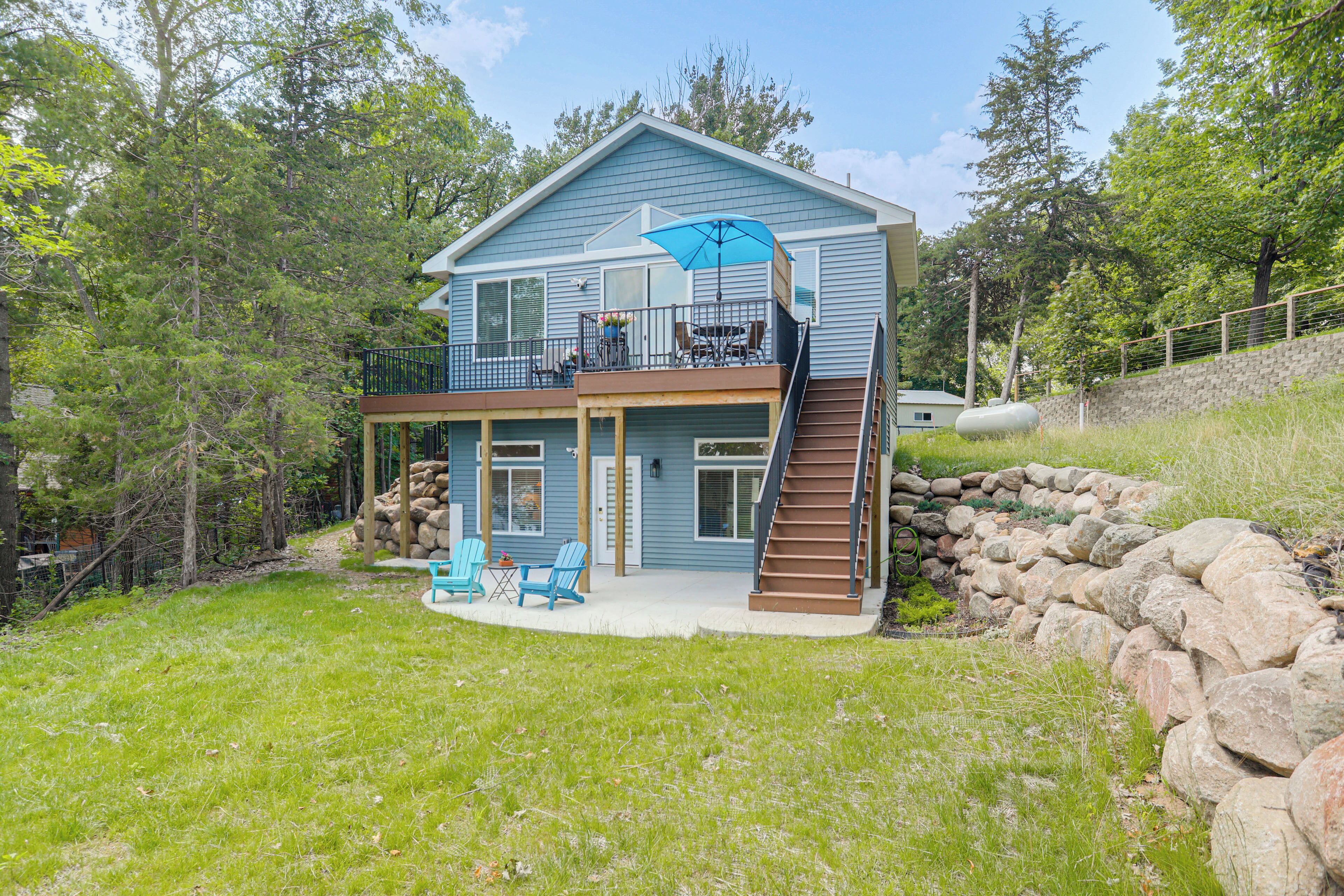 A two-story house with a balcony, a stone retaining wall, and a grassy yard.
