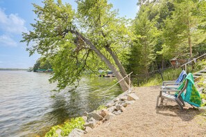 A lakeside seating area with a bench and a table, surrounded by trees and a rocky shoreline.