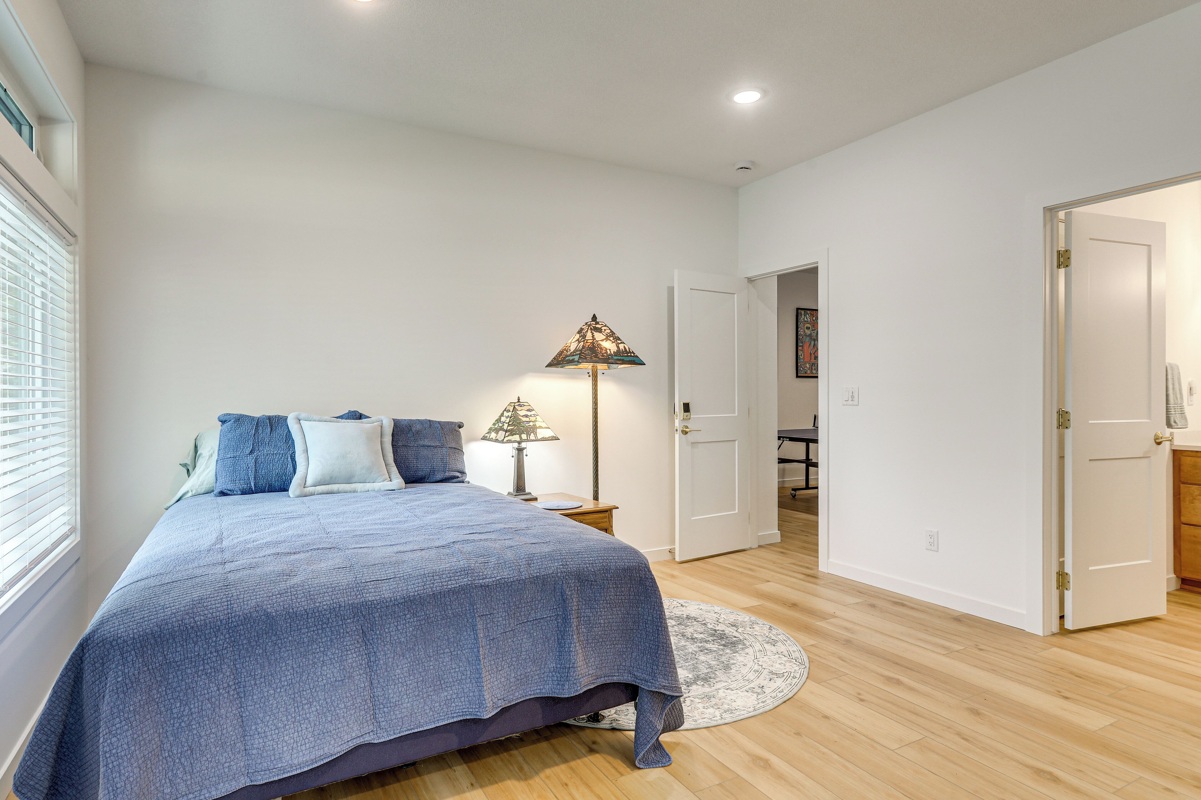 A bedroom with a bed, a bedside lamp, a round rug, and a door leading to another room.