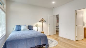 A bedroom with a bed, a bedside lamp, a round rug, and a door leading to another room.