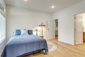 A bedroom with a bed, a bedside lamp, a round rug, and a door leading to another room.